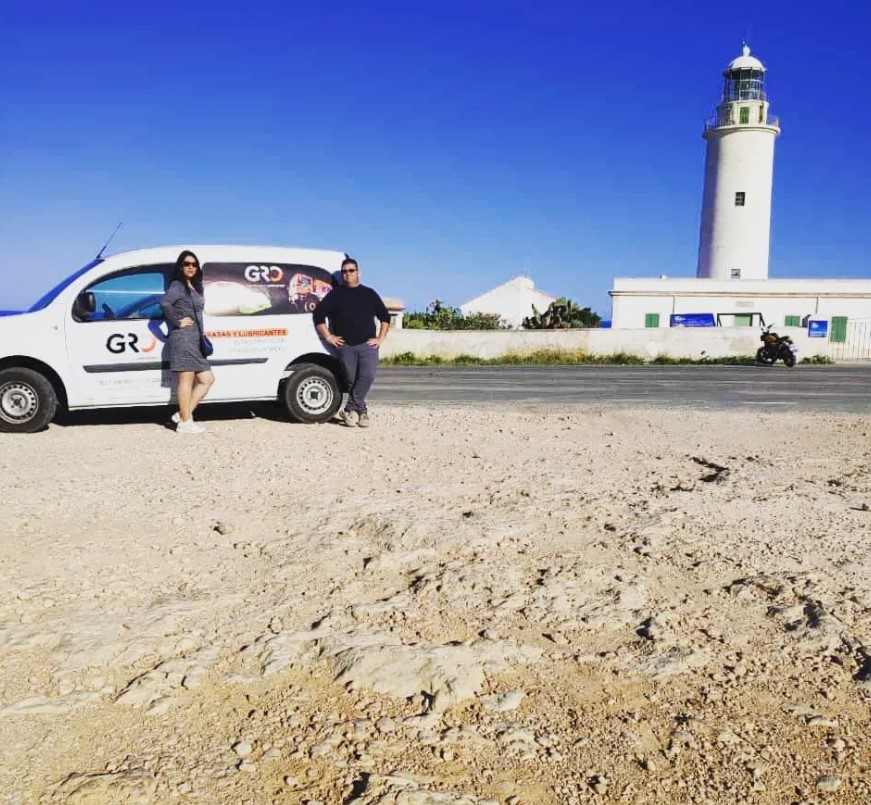 Distribuciones Gro Baleares furgoneta de empresa con jefes apoyados sobre ella y un faro de fondo